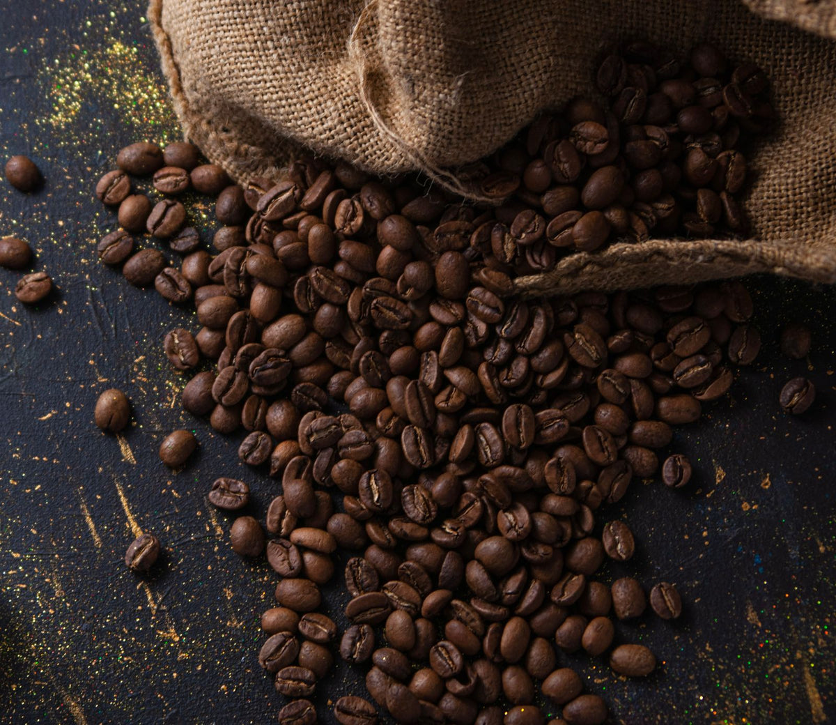Koffiebonen die uit een jute zak op tafel vallen