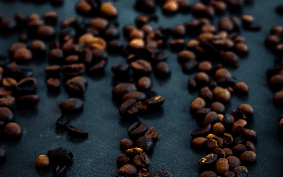 Donker gebrande koffiebonen verspreid over een donkere ondergrond