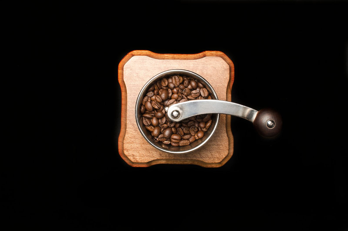 Een houten handmolen gevuld met gebrande koffiebonen, van boven gezien op een donkere achtergrond