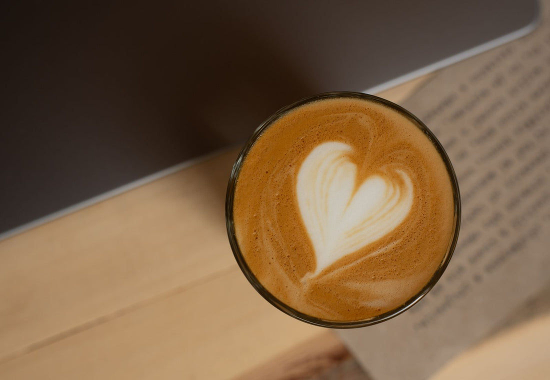Cortado met hartvormige latte art in een glas op een houten tafel
