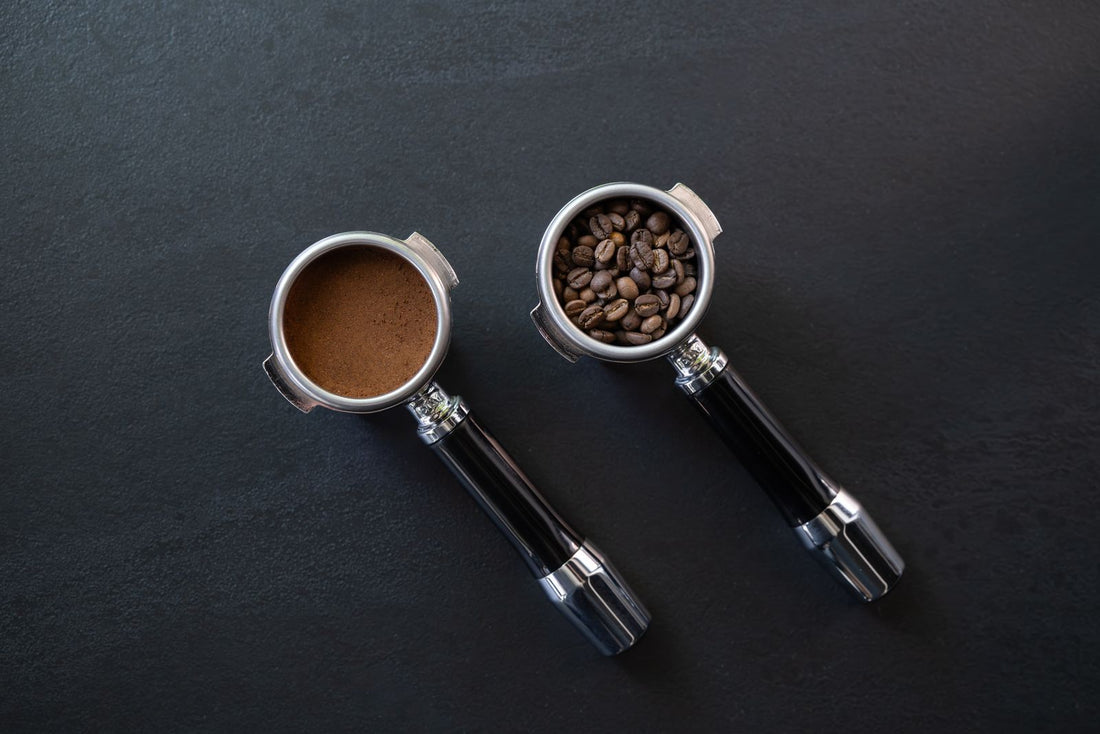 Twee filterdragers van een espressomachine op een donkere ondergrond, de een gevuld met hele koffiebonen, de ander met gemalen koffie