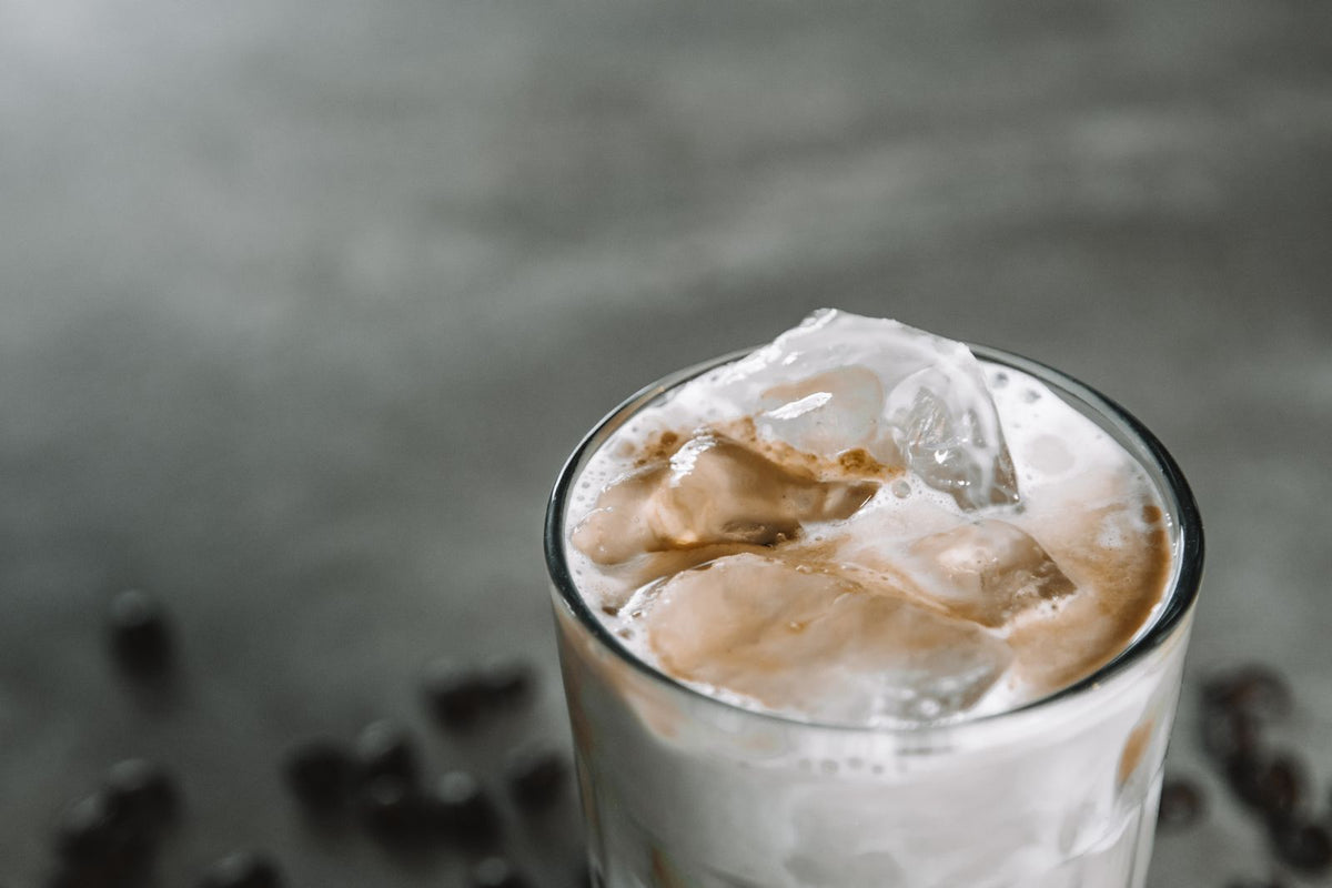 Glas ijskoffie met melk en ijsblokjes, omringd door koffiebonen op een donker oppervlak