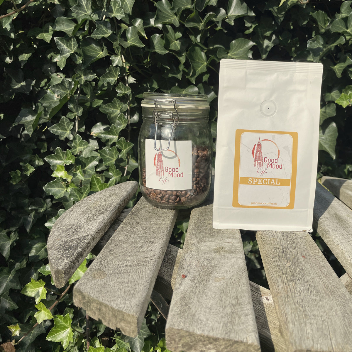 Zak Wisselende Special van Good Mood Coffee naast een glazen pot koffiebonen op een houten tuintafel