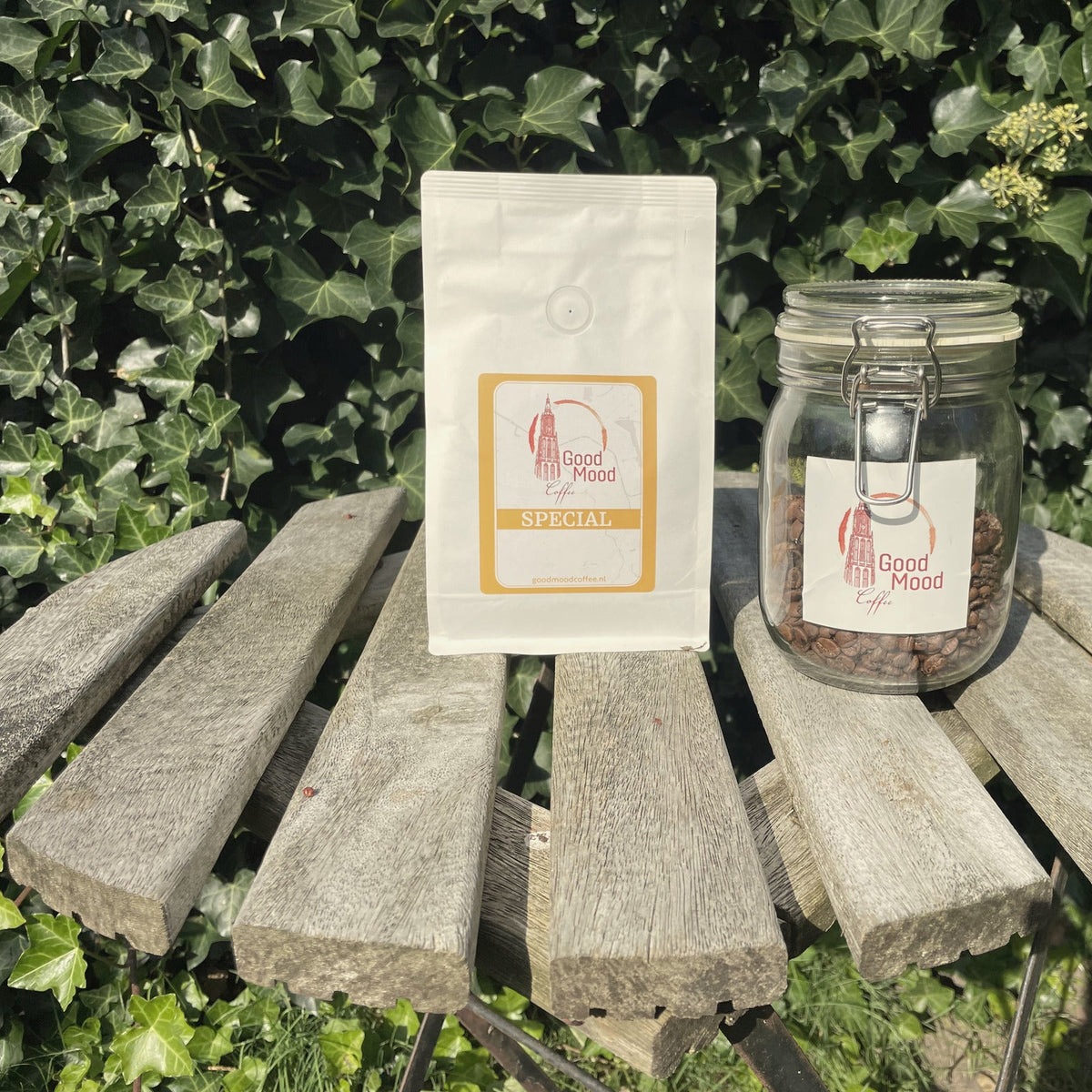 Glazen pot koffiebonen naast een zak Wisselende Special van Good Mood Coffee op een houten tuintafel