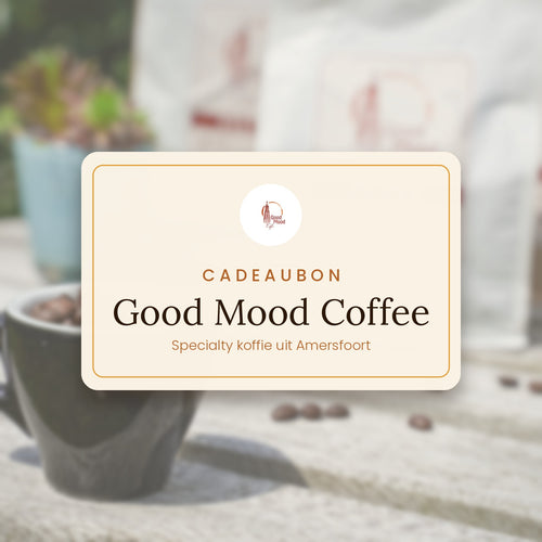 Cadeaubon van Good Mood Coffee op een houten tafel, met op de achtergrond een zwarte kop gevuld met koffiebonen